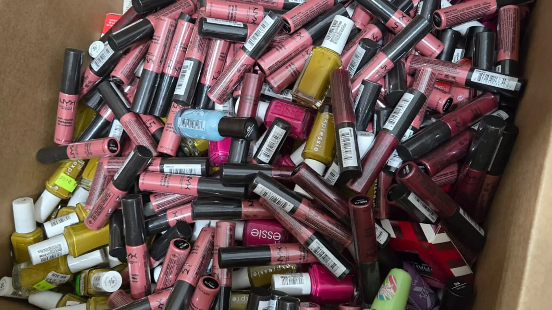 Close-up of assorted NYX and Essie cosmetic items inside a shelf-pull box